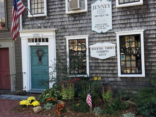 Exterior of the Jenney Museum with a green door, flower beds, and an American flag, showcasing historic tours and exhibits.