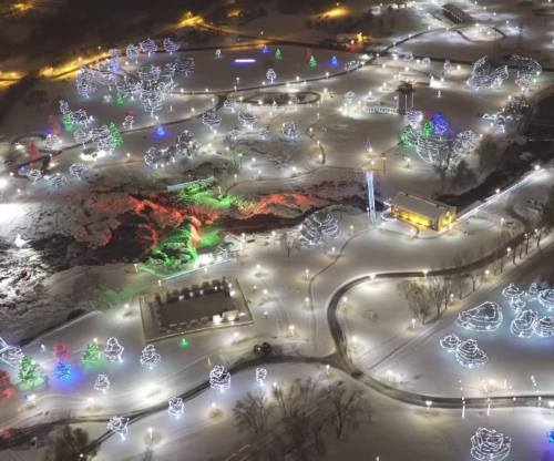 Aerial view of a snowy park decorated with colorful holiday lights and illuminated trees.