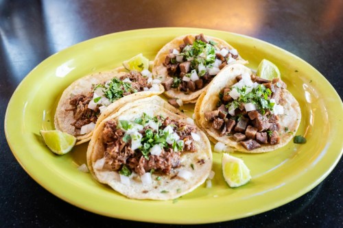 A vibrant plate of four tacos filled with beef, topped with onions and cilantro, served with lime wedges.