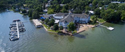 Aerial view of a lakeside resort with boats docked, surrounded by greenery and a sandy beach area.