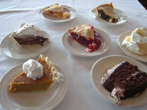 A variety of desserts on plates, including chocolate, cherry, pumpkin pie, and a slice of chocolate cake with whipped cream.