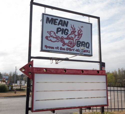 Sign for "Mean Pig BBQ" featuring a cartoon pig and the tagline "Home of the SHUT-UP-AND-EAT!" with a blank message board.