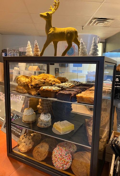 A display case filled with various baked goods, topped with a golden reindeer and small decorative trees.