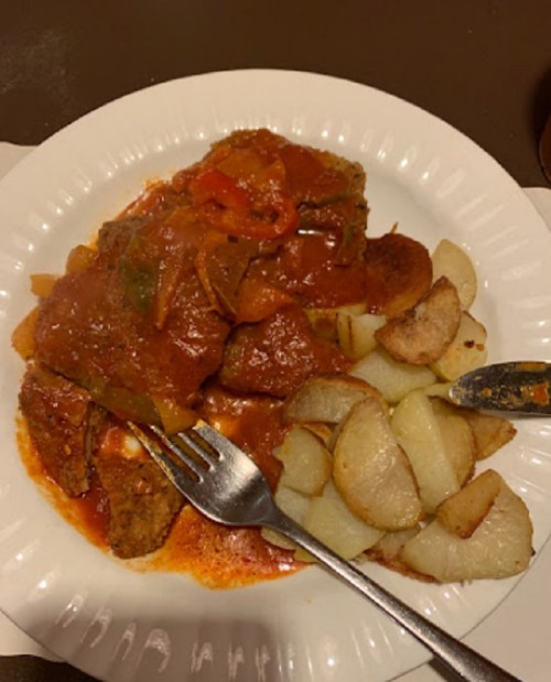 A plate of meat with tomato sauce and peppers, served with roasted potato wedges.