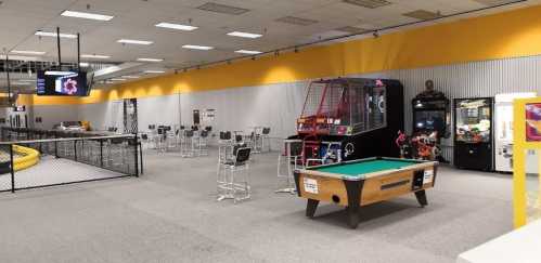 A spacious arcade with various games, including a pool table and claw machines, set against a bright yellow wall.