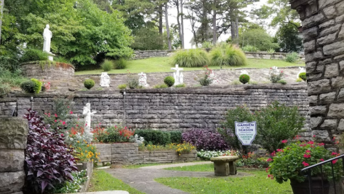 A serene garden with stone walls, statues, and colorful flowers, surrounded by greenery and trees.