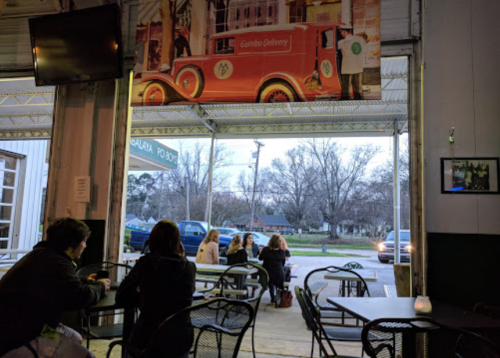 View from inside a casual eatery, showing patrons at tables and an open entrance with a vintage car mural above.
