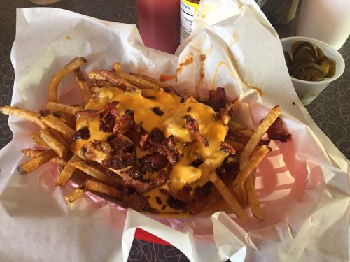 A basket of loaded fries topped with melted cheese and crispy bacon, served with ketchup and jalapeños on the side.