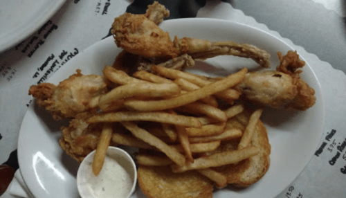A plate with two fried chicken drumsticks, a serving of French fries, and a small cup of dipping sauce.
