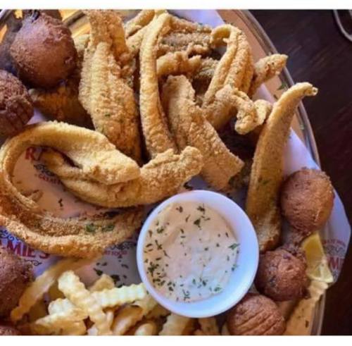 A platter of fried catfish strips, hushpuppies, crinkle-cut fries, and a small bowl of dipping sauce.