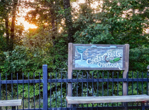 Sign for Cedar Falls Overlook with a scenic background of trees and a sunset.