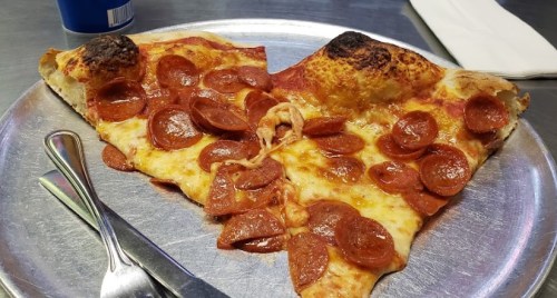 Two slices of pepperoni pizza on a silver plate, with melted cheese and a crispy crust. Fork and knife beside it.