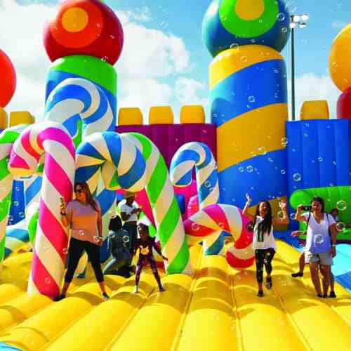 Colorful inflatable playground with candy-themed structures and children playing among bubbles.