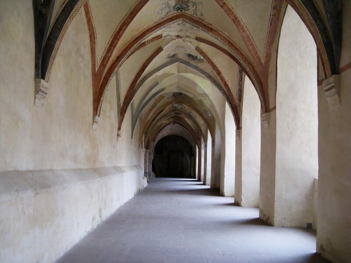 A long, empty corridor with arched ceilings and faded frescoes, creating a serene and historic atmosphere.