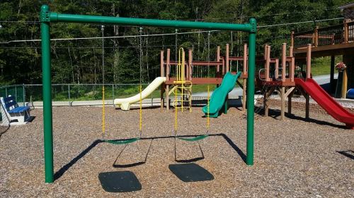 A playground featuring swings, slides, and climbing structures, surrounded by wood chips and greenery.
