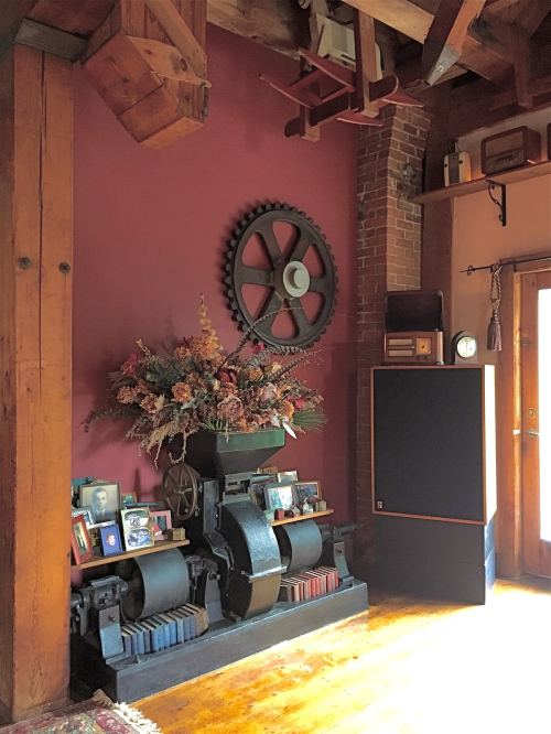 Cozy interior featuring a large gear on the wall, a floral arrangement, and a speaker beside framed photos.