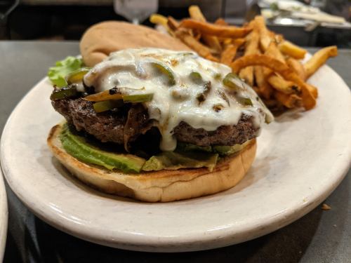 A juicy burger with melted cheese, lettuce, and grilled onions, served with a side of crispy French fries.