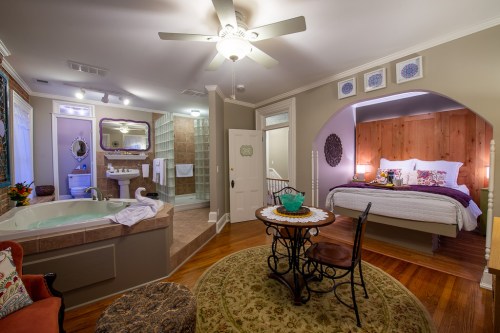 Cozy bedroom suite featuring a king bed, seating area, jacuzzi, and elegant decor in warm tones.