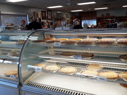 A display case filled with various pies, including pecan, blueberry, and cherry, in a cozy shop setting.
