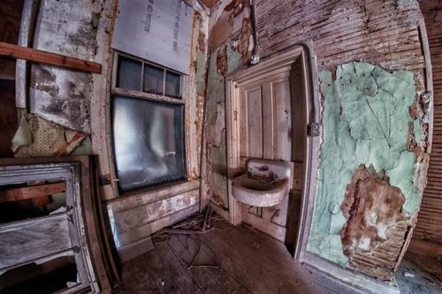 A dilapidated room with peeling paint, a sink, and a foggy window, showcasing signs of neglect and decay.