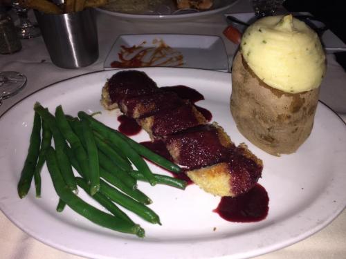 A plate featuring green beans, a breaded meat dish with berry sauce, and a baked potato topped with mashed potatoes.