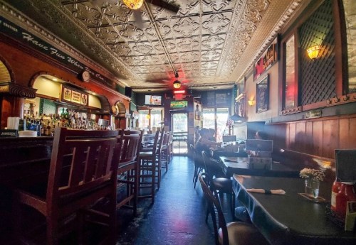 Cozy restaurant interior with wooden furniture, bar area, and decorative ceiling, featuring dim lighting and a welcoming atmosphere.