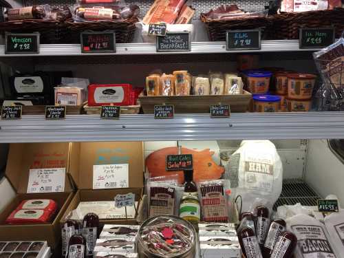 A display case filled with various meats, cheeses, and snacks, each labeled with prices on small black signs.