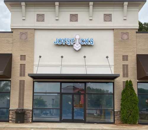 Exterior of a building with the sign "Joysticks" above the entrance, featuring large windows and a brick facade.