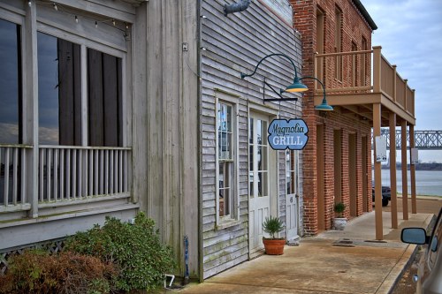 Exterior view of Magnolia Grill, featuring a wooden facade and brick building, near a waterfront.