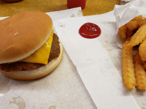 A cheeseburger with a slice of cheese and a side of crinkle-cut fries with ketchup on a paper tray.