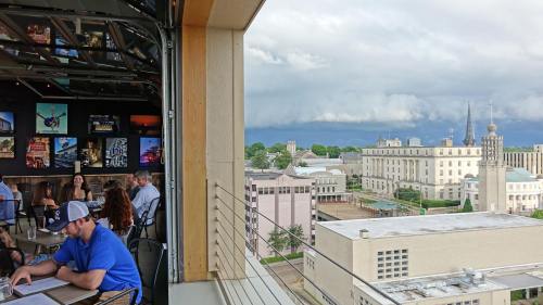 A rooftop view of a city with stormy clouds, featuring diners enjoying a meal indoors.