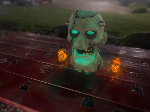 A glowing zombie skull centerpiece with two small illuminated skulls on a red table at night.