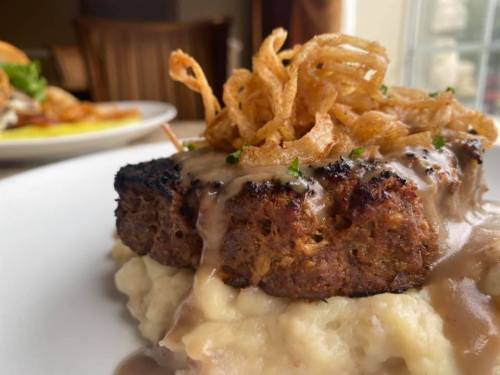 A close-up of meatloaf topped with gravy and crispy onions, served on a bed of creamy mashed potatoes.