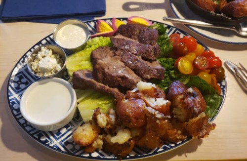 A platter featuring sliced steak, lettuce, cherry tomatoes, and crispy potatoes, with dipping sauces on the side.
