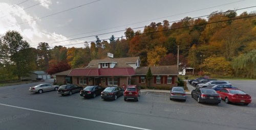 A restaurant with a red roof surrounded by trees in autumn colors, with several cars parked in front.