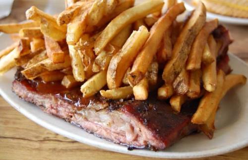 A plate of juicy barbecue ribs topped with a generous serving of golden French fries.