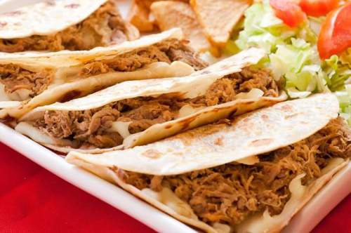 A plate of tacos filled with shredded meat, served with tortilla chips and a side of lettuce and tomato.