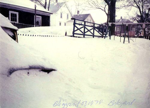 A snowy backyard scene from a blizzard in 1970, with deep snow covering the ground and a wooden gate in the background.