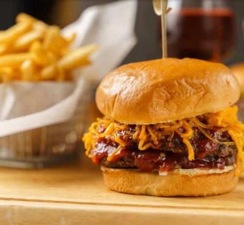 A close-up of a juicy burger topped with melted cheese and barbecue sauce, served with a side of golden fries.