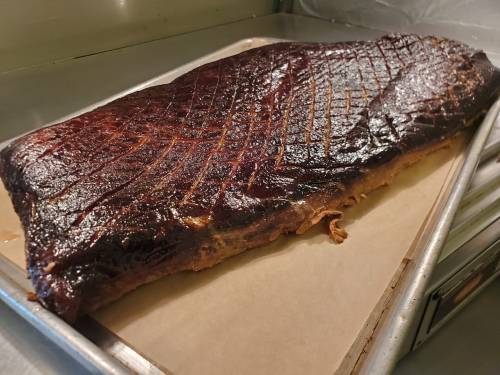 A large, smoked brisket resting on a baking sheet, showcasing a dark, caramelized crust.