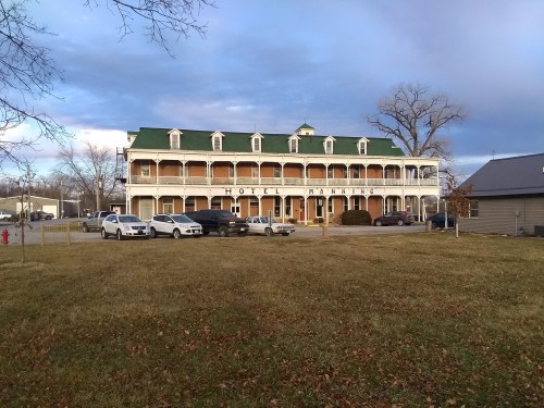 Historic hotel with a green roof, multiple balconies, and parked cars in front, set against a cloudy sky.