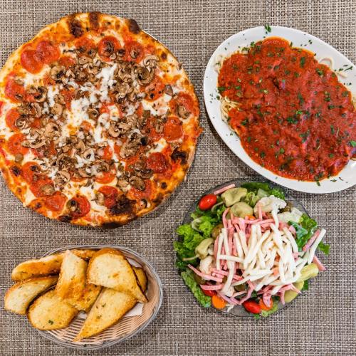 A spread of pizza with mushrooms and pepperoni, spaghetti with marinara, a salad, and garlic bread on a textured table.