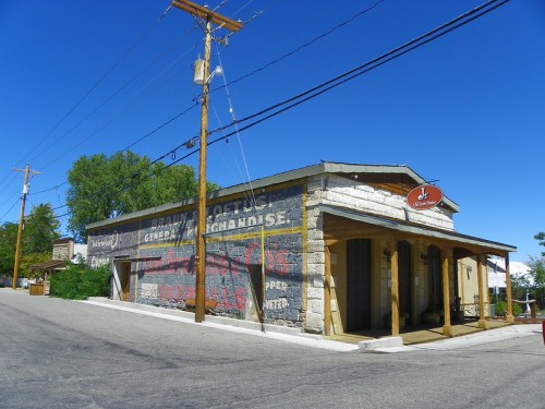 A historic general store with a faded mural, set against a clear blue sky and power lines in a small town.
