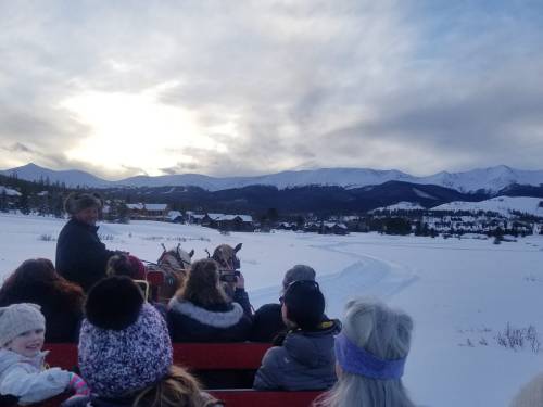 A group of people on a sleigh ride through snowy mountains, with a scenic view of the landscape and cloudy sky.