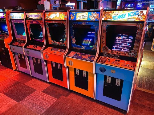 A row of classic arcade game machines, including Donkey Kong and others, in a vibrant gaming venue.