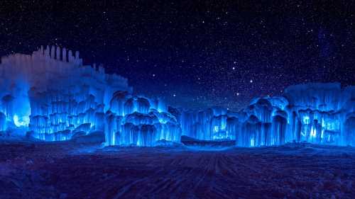 A stunning night scene of illuminated ice formations under a starry sky, glowing in shades of blue.