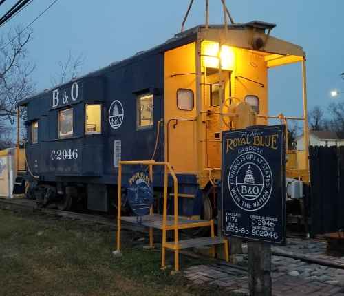 A blue and yellow caboose with a sign, set against a twilight sky, showcasing its historical significance.