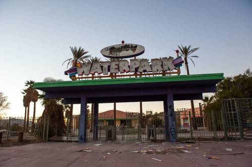 Abandoned waterpark entrance with colorful signage, surrounded by palm trees and scattered debris.