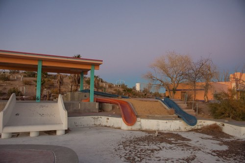 Abandoned playground with two slides, a sandy area, and a colorful structure under a twilight sky.
