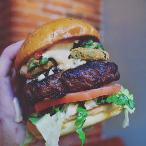 A hand holding a juicy burger with a grilled patty, lettuce, tomato, and a creamy sauce, all in a shiny bun.